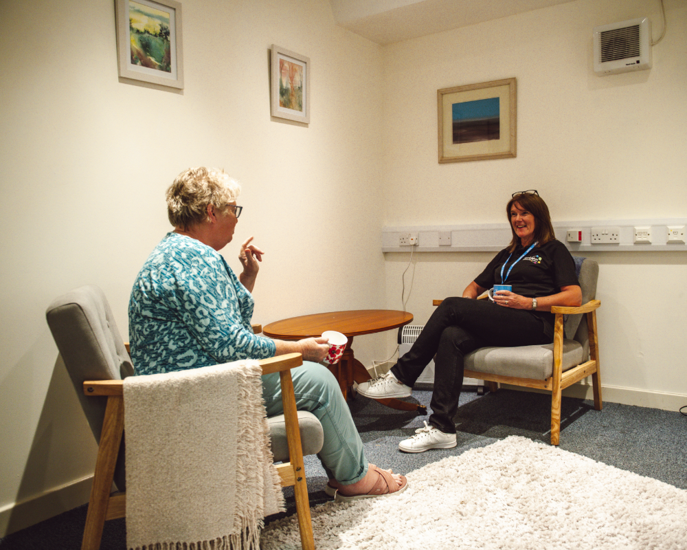 two women in a room talking with cups of tea and sat in chairs opposite eachother